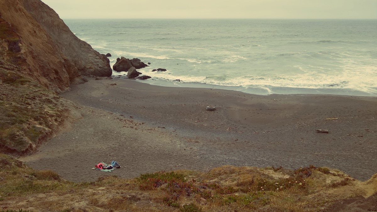 Two people laying on a towel on a beach, seen from far away.