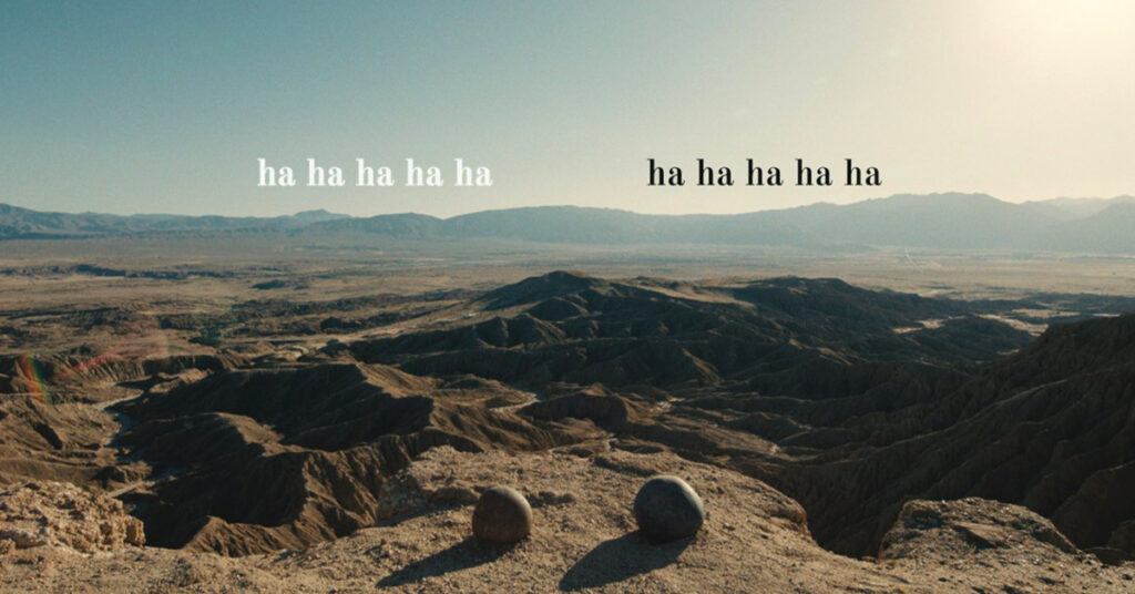 Two round rocks sitting at the edge of a beautiful canyon view with speech text indicating that both the rocks are laughing.