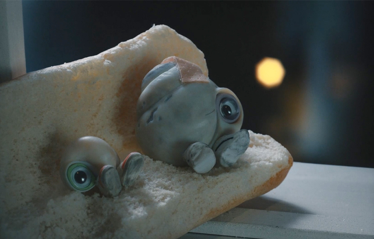 A screenshot of Marcel the Shell sitting on a couch made out of bread next to his grandma, Nanna Connie.