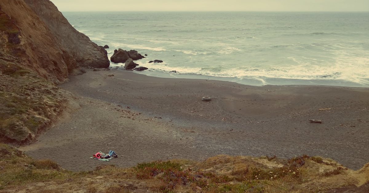 Two people laying on a towel on a beach, seen from far away.